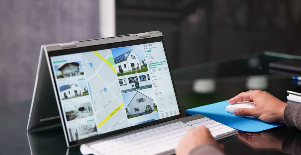 Personne vue de profil consultant une carte de quartiers et des documents immobiliers étalés sur une table de travail à domicile