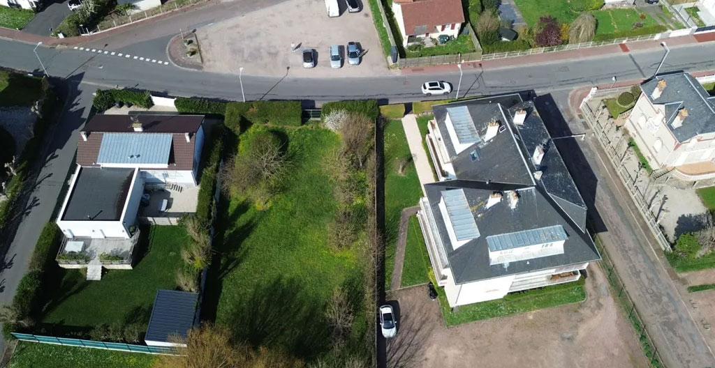 Personne marchant de dos dans une rue résidentielle bordée d'arbres et de jardins à Pont-Audemer