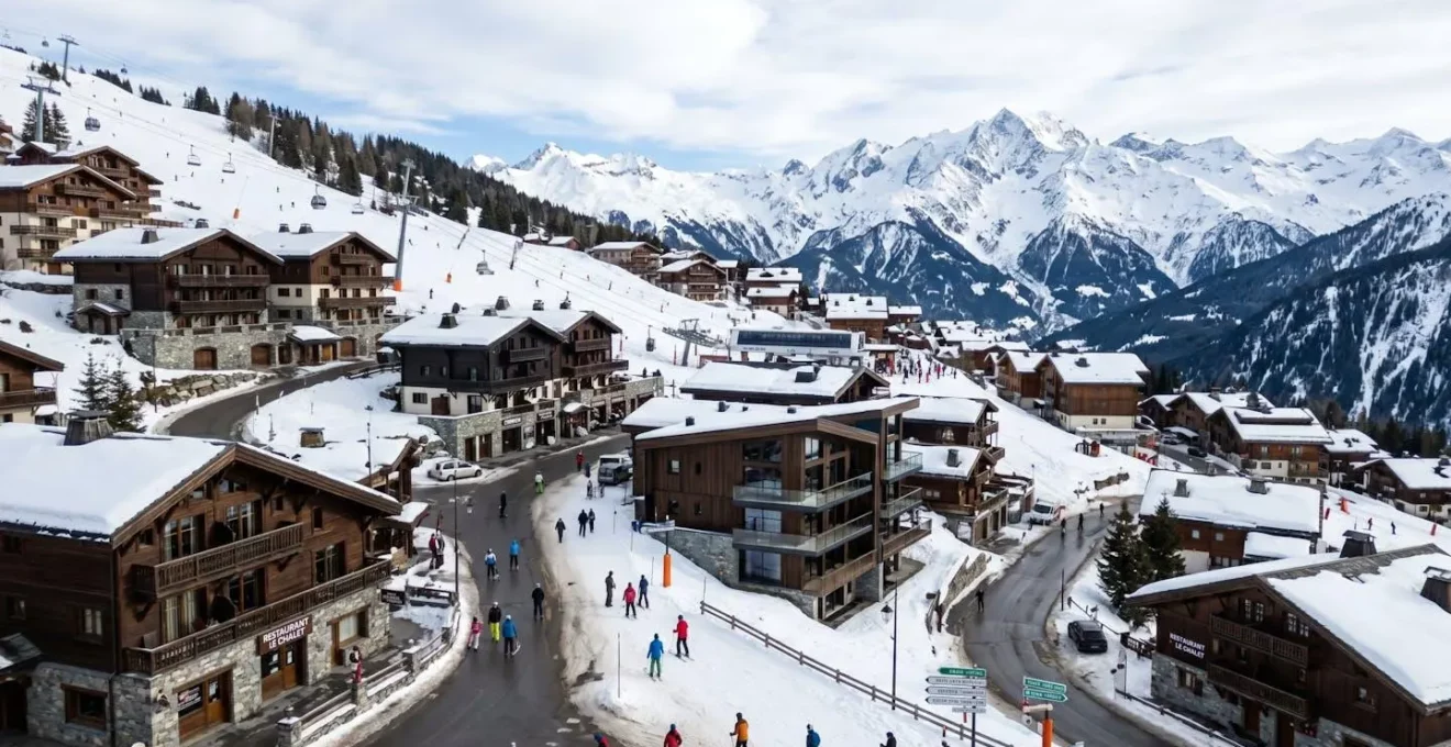 Vue panoramique d'un village de Courchevel montrant des chalets savoyards à différents niveaux d'altitude avec sommets alpins enneigés en arrière-plan